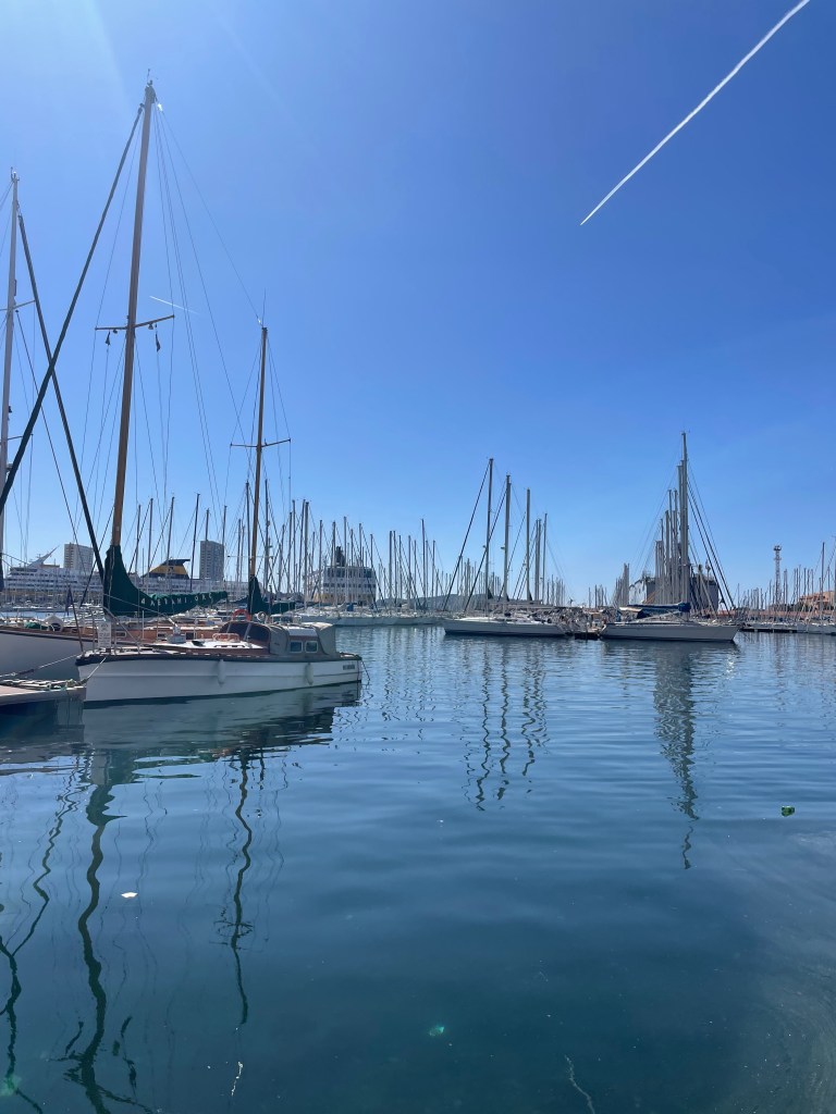 Pohled na přístav v Toulonu s plachetními loděmi a modrou oblohou.