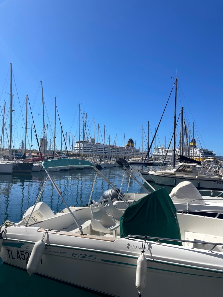 Marina v Toulonu se středními a velkými loděmi, modrou oblohou a slunečním svitem.